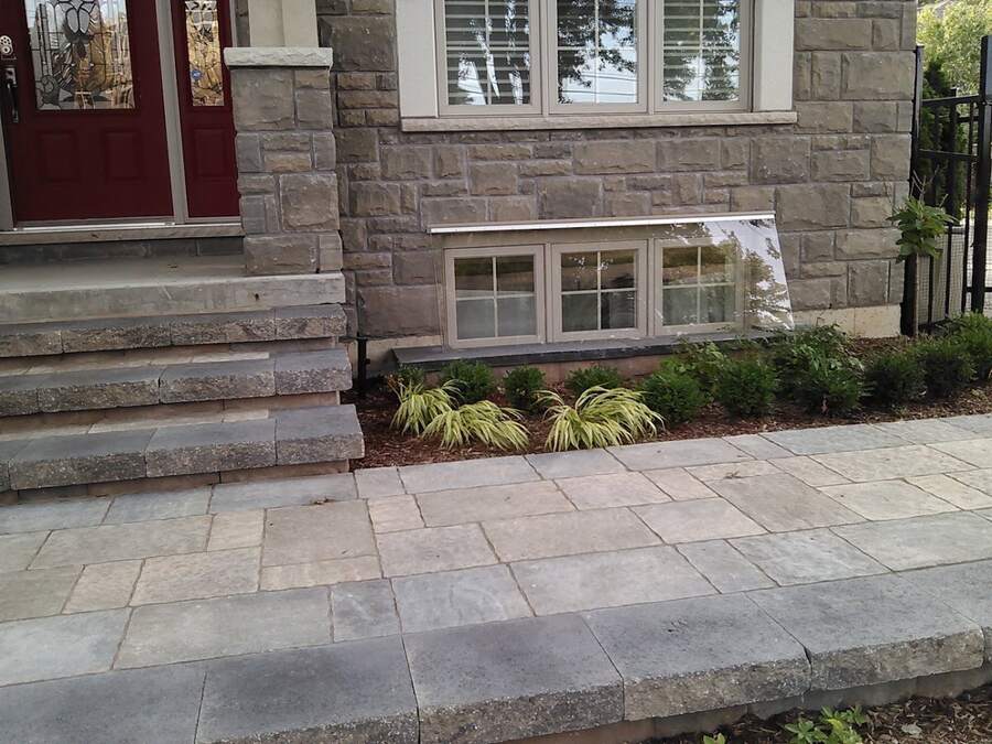 Low-profile clear basement window well cover installed at a stone-front home