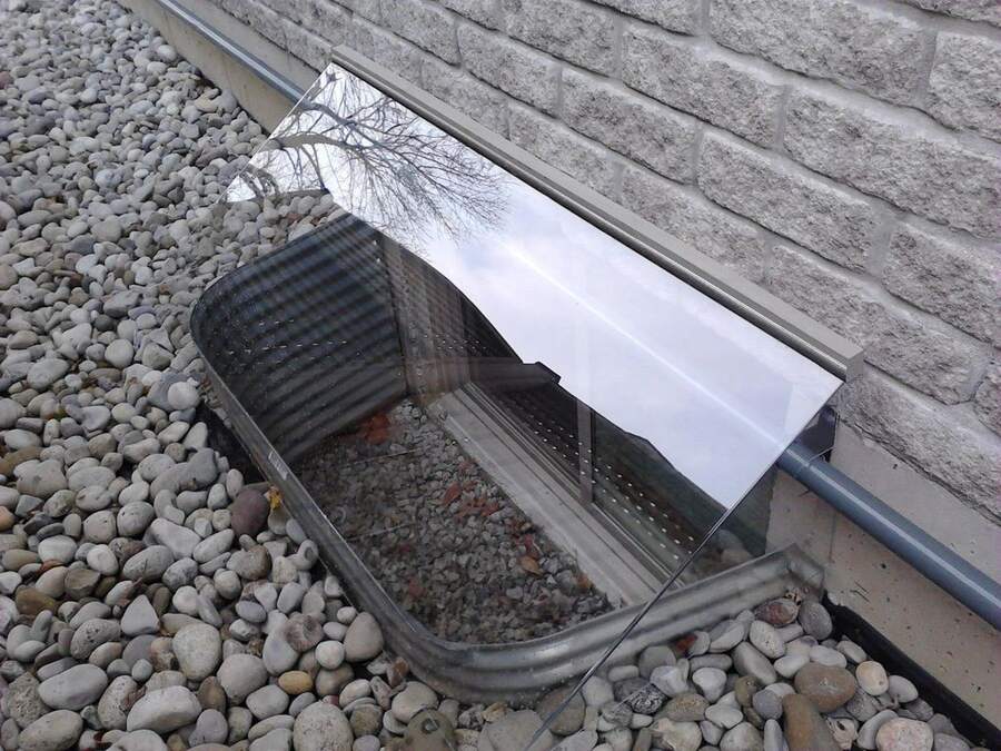 Hinged custom window well cover installed over a deep basement well